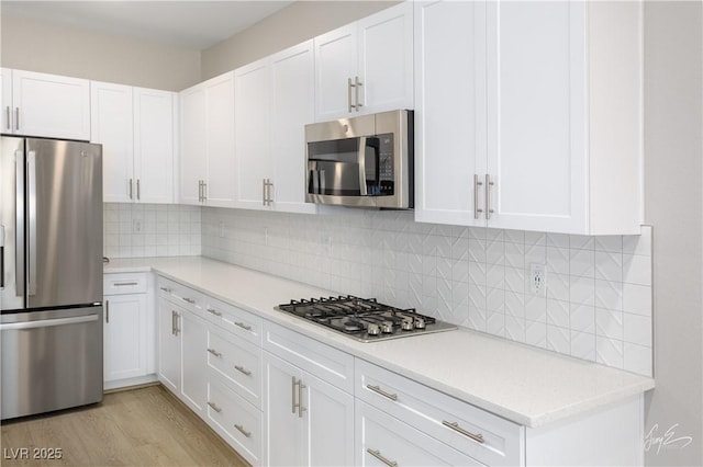 kitchen featuring decorative backsplash, stainless steel appliances, white cabinets, and light wood-type flooring