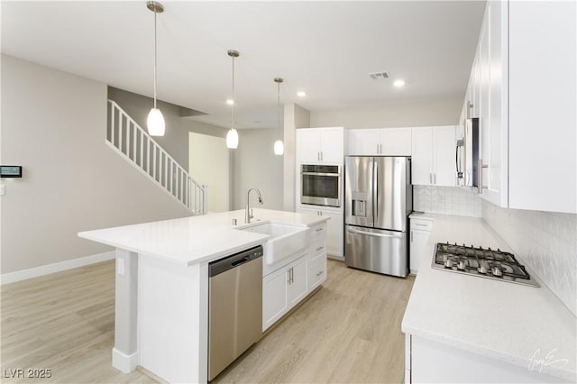 kitchen featuring pendant lighting, appliances with stainless steel finishes, white cabinetry, an island with sink, and decorative backsplash