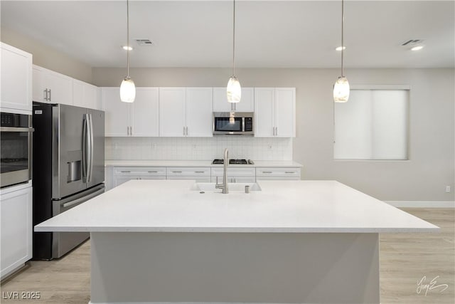 kitchen featuring appliances with stainless steel finishes, hanging light fixtures, a center island with sink, and white cabinets