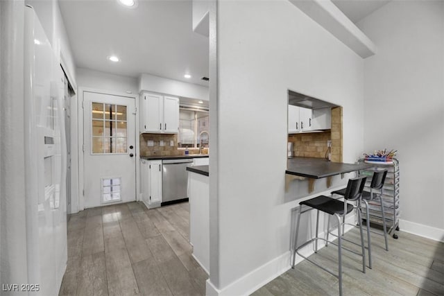 kitchen featuring white cabinetry, stainless steel dishwasher, a kitchen breakfast bar, light hardwood / wood-style floors, and backsplash