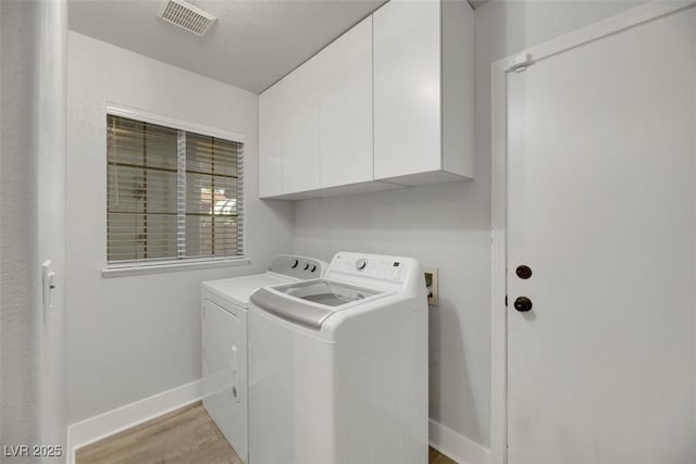 washroom with light hardwood / wood-style flooring, washing machine and dryer, and cabinets