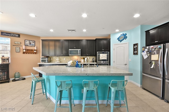 kitchen with light stone counters, a breakfast bar area, an island with sink, and appliances with stainless steel finishes