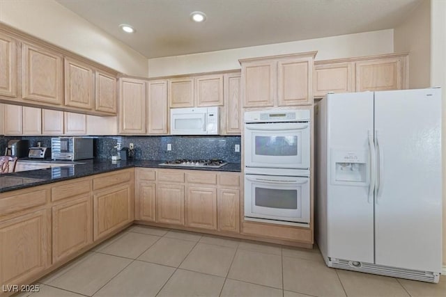 kitchen featuring tasteful backsplash, dark stone counters, light tile patterned floors, light brown cabinets, and white appliances