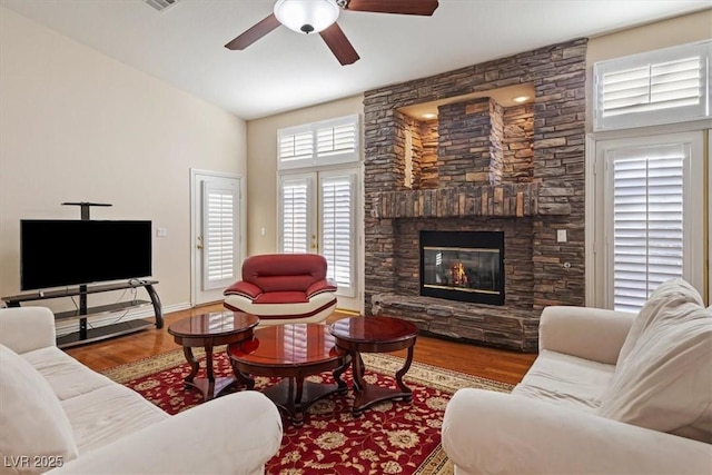 living room featuring ceiling fan, wood-type flooring, a fireplace, and a towering ceiling