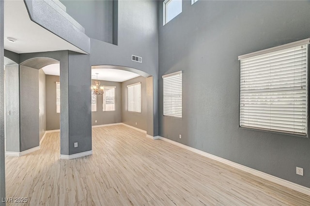 empty room featuring a towering ceiling, a notable chandelier, and light hardwood / wood-style flooring