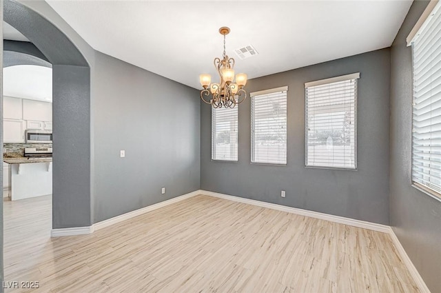 spare room with a notable chandelier and light wood-type flooring