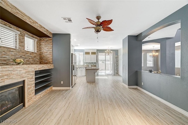 unfurnished living room featuring ceiling fan with notable chandelier, a fireplace, plenty of natural light, and light wood-type flooring