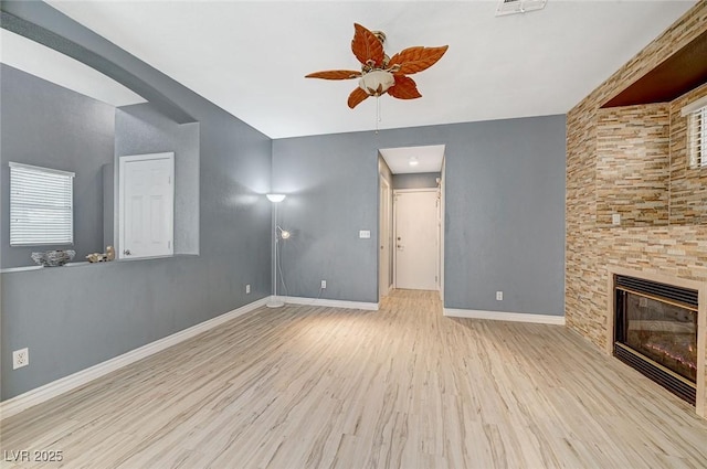 unfurnished living room with ceiling fan, a stone fireplace, and light hardwood / wood-style floors