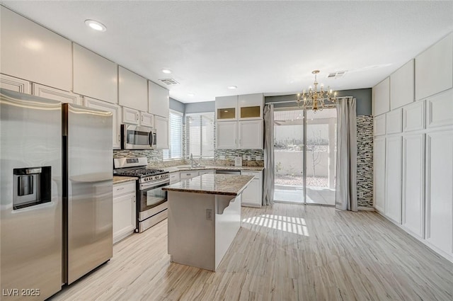 kitchen featuring a center island, hanging light fixtures, stainless steel appliances, decorative backsplash, and white cabinets