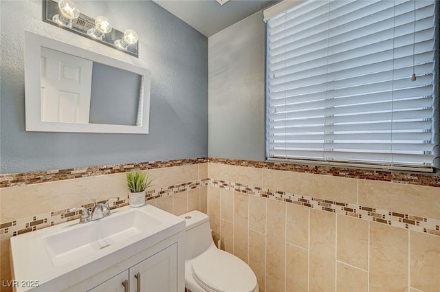 bathroom featuring vanity, toilet, and tile walls