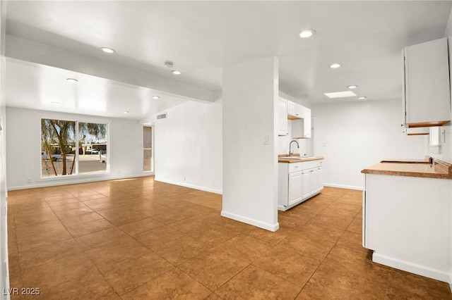 kitchen featuring white cabinetry, sink, light tile patterned floors, and beam ceiling