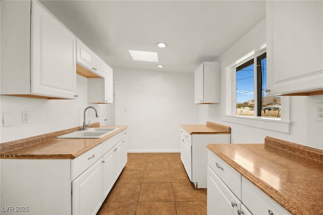 kitchen with white cabinetry, sink, light tile patterned floors, and a skylight