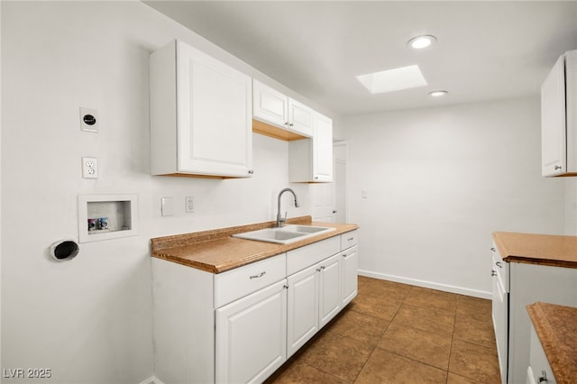 kitchen with sink, dark tile patterned floors, a skylight, and white cabinets