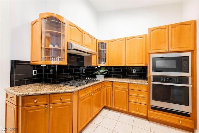 kitchen featuring tasteful backsplash, light tile patterned flooring, light stone countertops, and appliances with stainless steel finishes