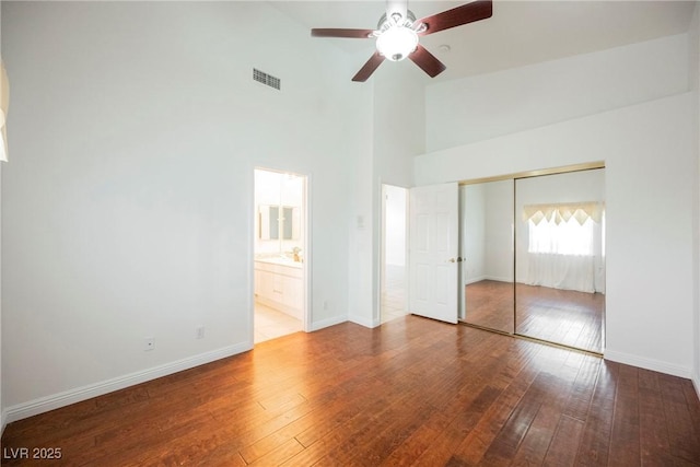 unfurnished bedroom with ensuite bath, hardwood / wood-style flooring, ceiling fan, high vaulted ceiling, and a closet