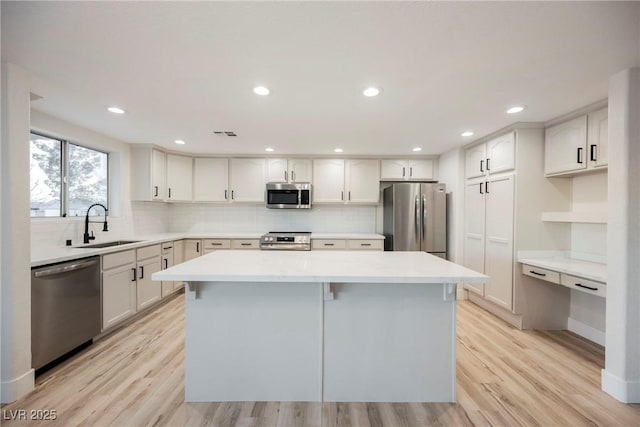 kitchen with appliances with stainless steel finishes, a center island, sink, and light wood-type flooring