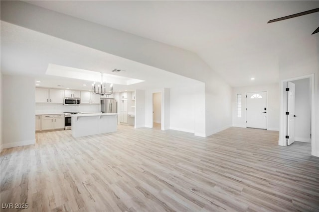 unfurnished living room with a notable chandelier, vaulted ceiling, and light wood-type flooring