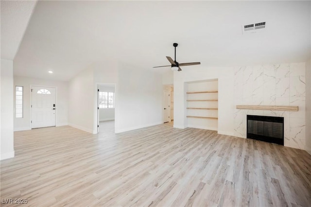 unfurnished living room with lofted ceiling, built in features, ceiling fan, a high end fireplace, and light hardwood / wood-style floors