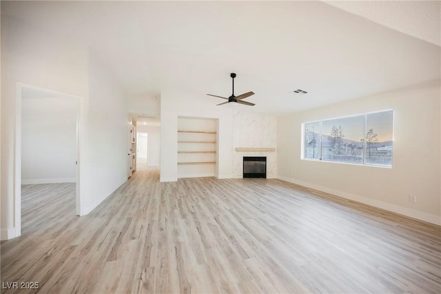 unfurnished living room with built in shelves, ceiling fan, a high end fireplace, and light wood-type flooring