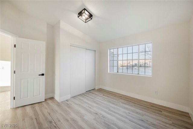 unfurnished bedroom with vaulted ceiling, light hardwood / wood-style floors, and a closet