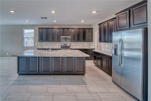 kitchen with sink, a kitchen island with sink, stainless steel appliances, and dark brown cabinetry