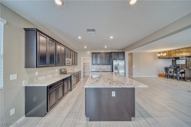 kitchen with sink, a center island with sink, appliances with stainless steel finishes, and light stone countertops