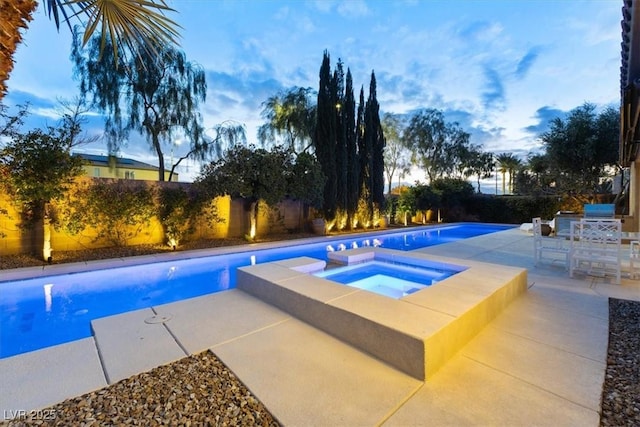 pool at dusk with an in ground hot tub and a patio