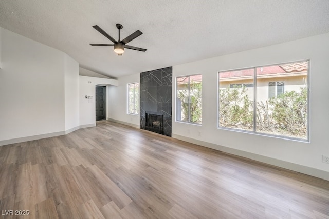 unfurnished living room with lofted ceiling, a textured ceiling, light wood-type flooring, ceiling fan, and a fireplace