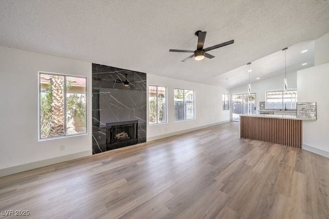 unfurnished living room featuring lofted ceiling, hardwood / wood-style flooring, ceiling fan, a high end fireplace, and a textured ceiling