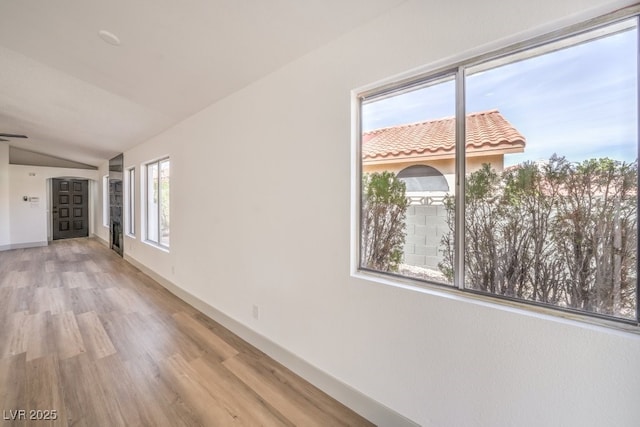 spare room with a wealth of natural light, vaulted ceiling, and light wood-type flooring