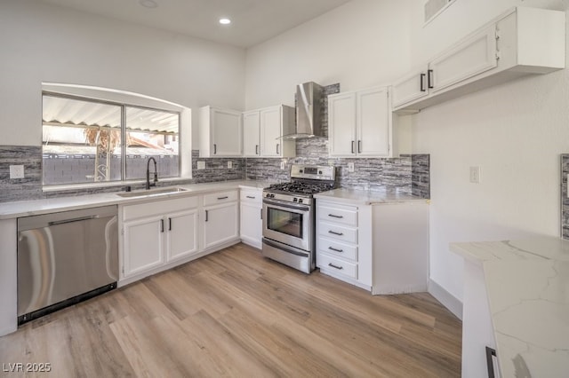 kitchen featuring wall chimney range hood, sink, white cabinets, and appliances with stainless steel finishes