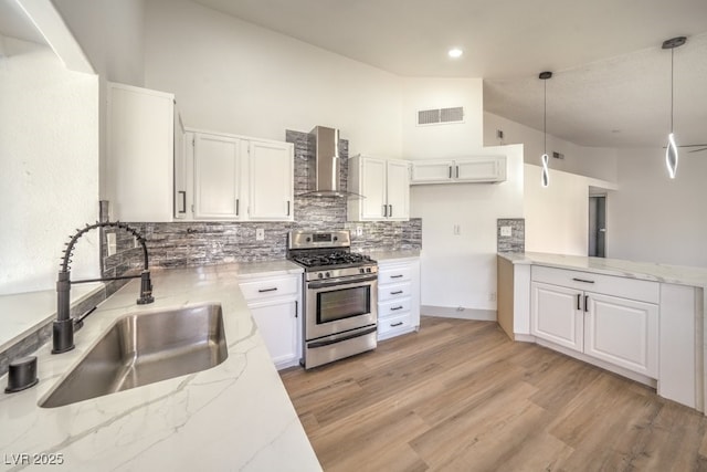 kitchen featuring wall chimney exhaust hood, sink, stainless steel gas stove, hanging light fixtures, and white cabinets