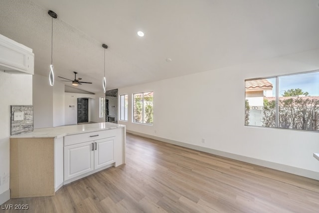 kitchen featuring light stone counters, vaulted ceiling, hanging light fixtures, and white cabinets