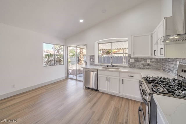 kitchen featuring appliances with stainless steel finishes, sink, white cabinets, light stone counters, and wall chimney range hood