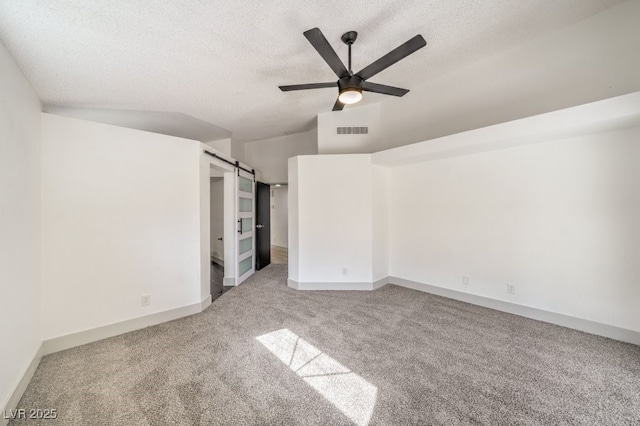 unfurnished bedroom featuring carpet flooring, ceiling fan, a barn door, and a textured ceiling