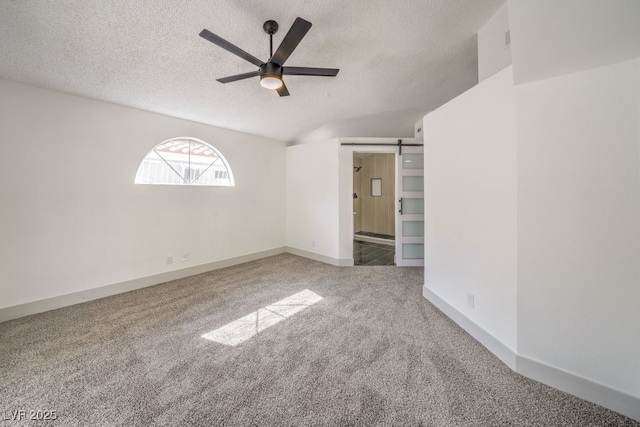 spare room with ceiling fan, carpet flooring, a barn door, and a textured ceiling