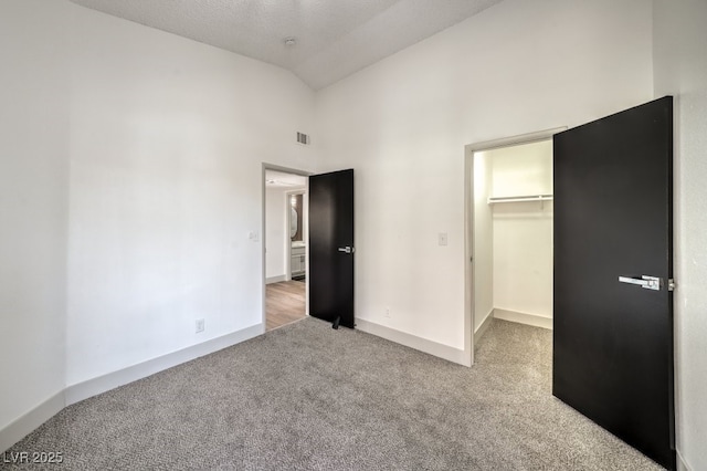 unfurnished bedroom featuring a spacious closet, high vaulted ceiling, a textured ceiling, a closet, and carpet