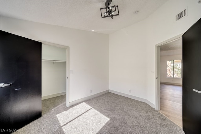 unfurnished bedroom featuring a walk in closet, light colored carpet, a closet, and a textured ceiling