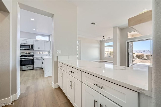 kitchen with kitchen peninsula, white cabinets, light hardwood / wood-style floors, light stone counters, and stainless steel appliances