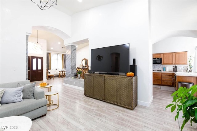 living room with sink, light hardwood / wood-style flooring, and a high ceiling