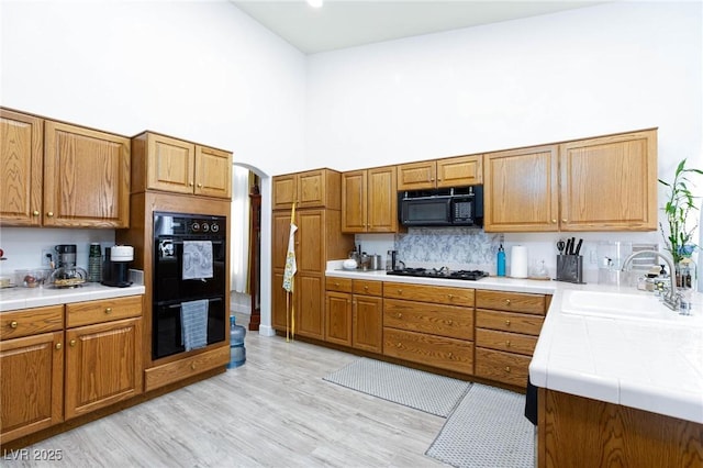 kitchen with sink, a towering ceiling, black appliances, light hardwood / wood-style floors, and decorative backsplash