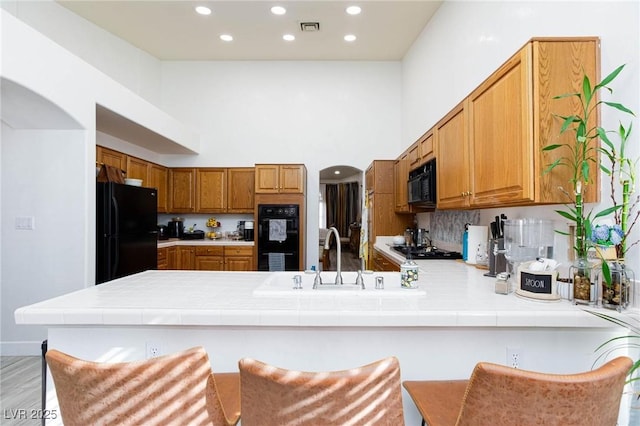 kitchen featuring black appliances, sink, a kitchen breakfast bar, tile counters, and kitchen peninsula