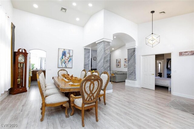 dining room featuring a towering ceiling, ornate columns, and light wood-type flooring