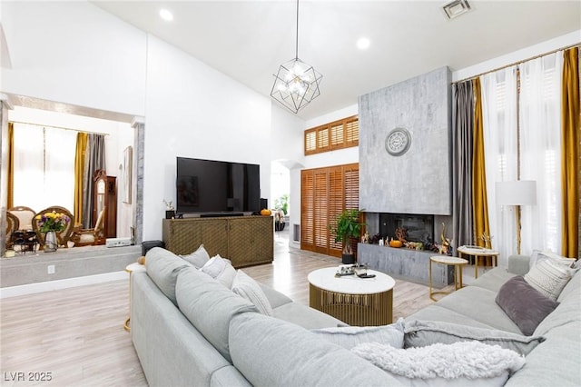 living room with a fireplace, high vaulted ceiling, a chandelier, and light wood-type flooring