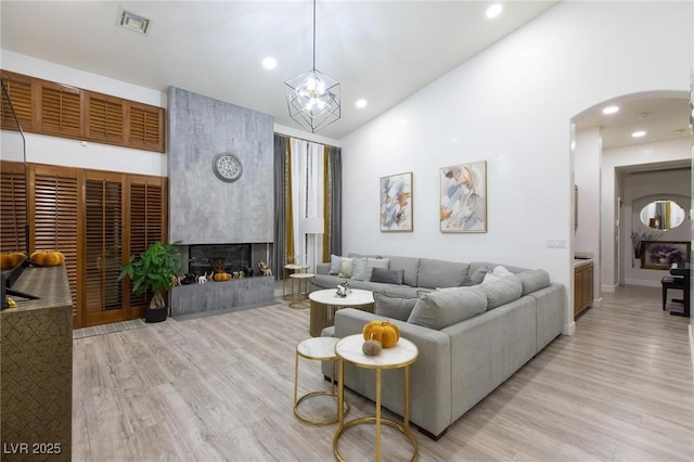 living room with high vaulted ceiling, a high end fireplace, and light hardwood / wood-style flooring