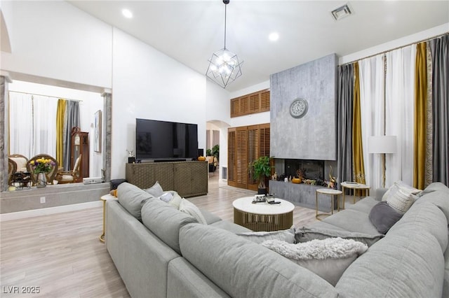 living room with a premium fireplace, a chandelier, high vaulted ceiling, and light wood-type flooring