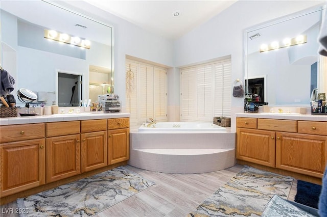 bathroom with vanity, tiled tub, and wood-type flooring