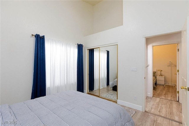 bedroom with multiple windows, a towering ceiling, light hardwood / wood-style floors, and a closet