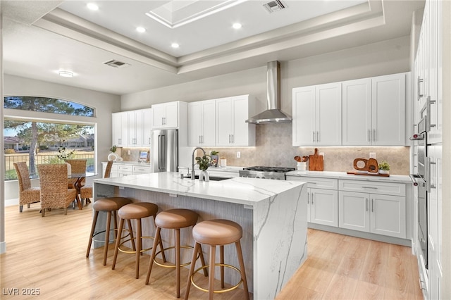 kitchen with sink, white cabinets, a kitchen island with sink, high end fridge, and wall chimney exhaust hood