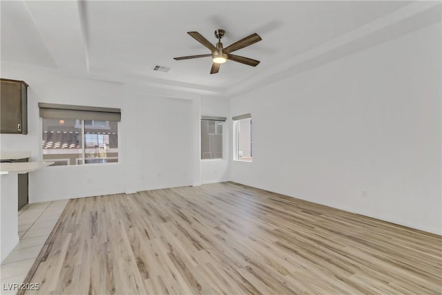 unfurnished living room featuring ceiling fan, a tray ceiling, and light hardwood / wood-style flooring